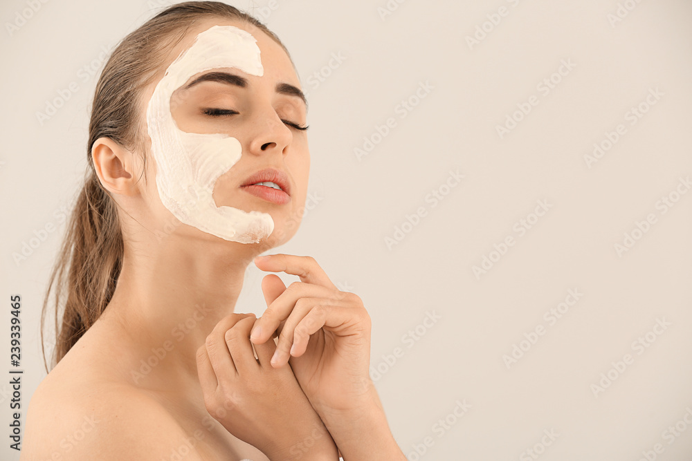 Beautiful young woman with facial mask on light background