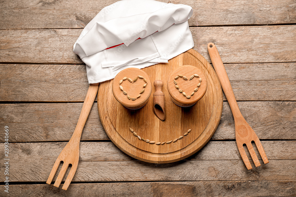 Creative composition with chefs hat, cutting board and kitchen utensils on wooden background