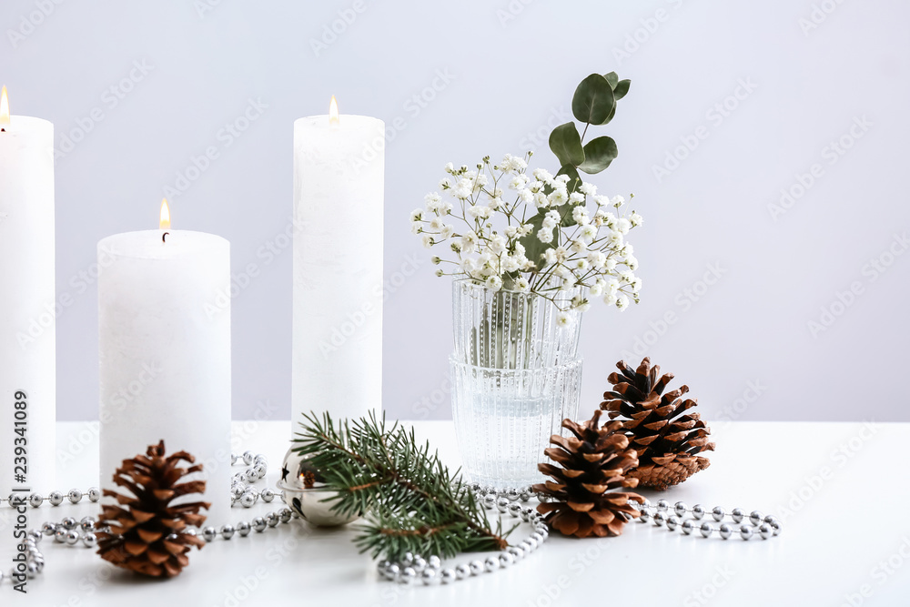 Beautiful burning candles with Christmas decor on white table