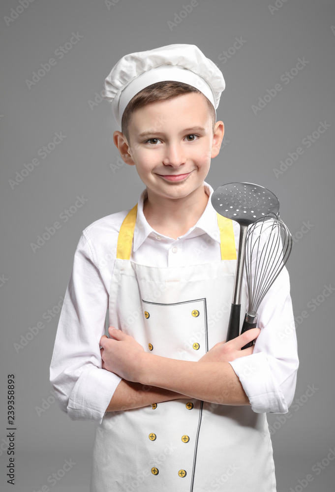 Cute little chef with kitchen utensils on grey background