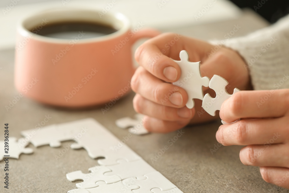 Woman assembling puzzle on table, closeup