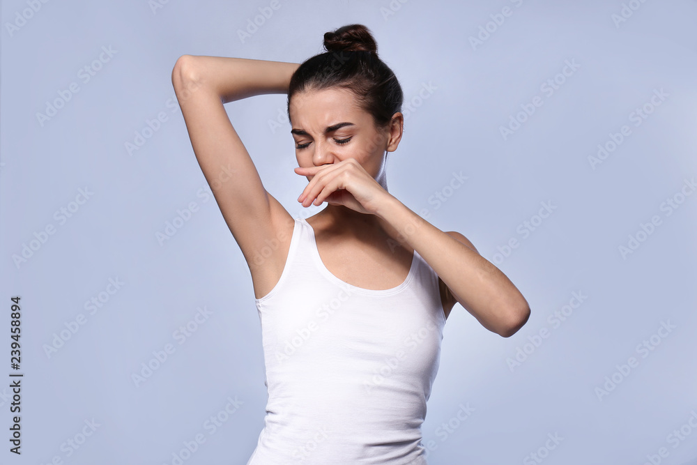 Beautiful young woman feeling smell of sweat on color background. Concept of using deodorant