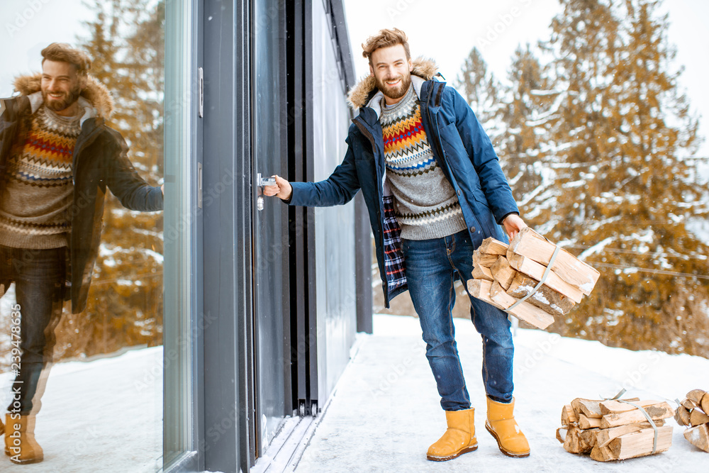 Man in winter clothes entering home carrying firewoods in the mountains