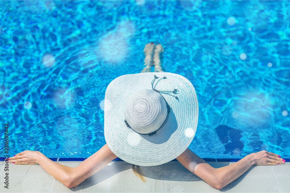 Beautiful woman in a hat sitting on the edge of the swimming