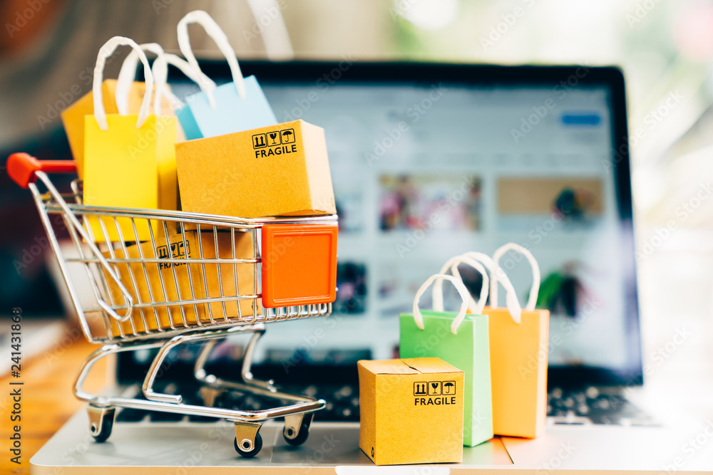 Product package boxes and shopping bag in cart with laptop computer which web store shop on screen f