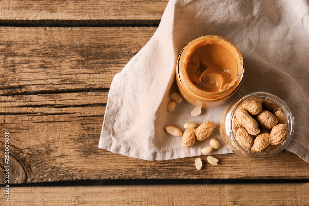 Jars with tasty peanut butter and nuts on wooden table