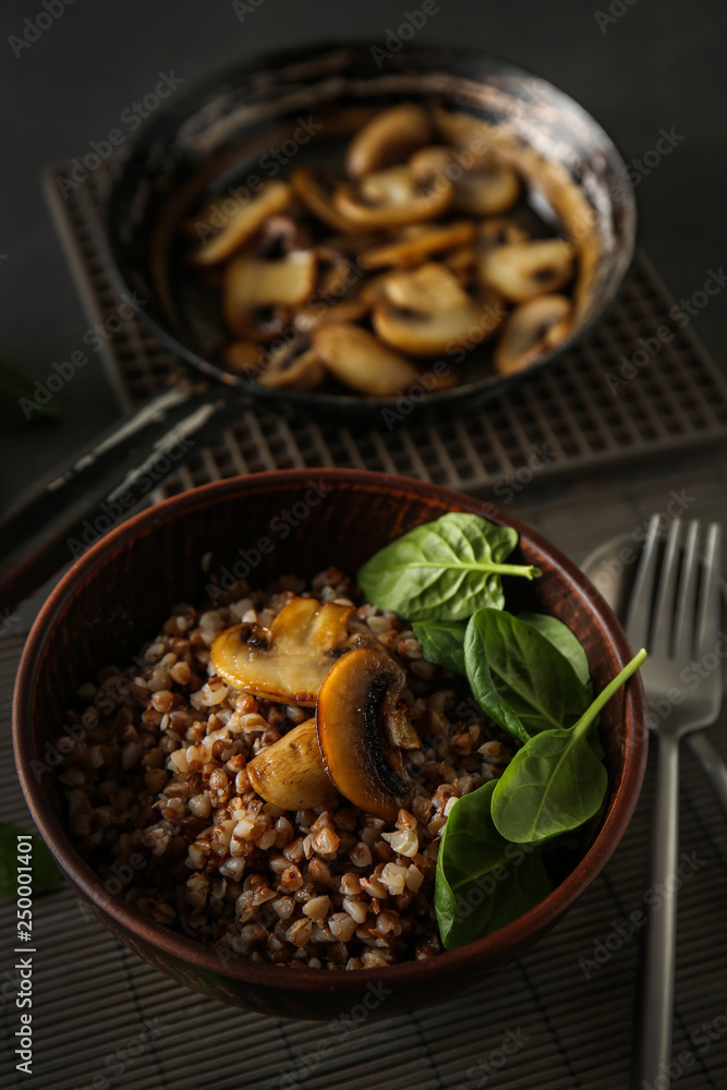 Bowl with tasty boiled buckwheat and fried mushrooms on table