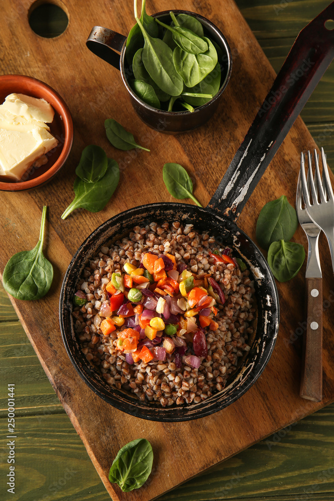 Frying pan with tasty boiled buckwheat and vegetables on wooden table