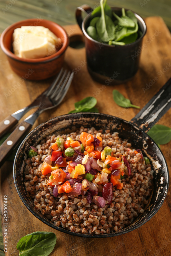 Frying pan with tasty boiled buckwheat and vegetables on table