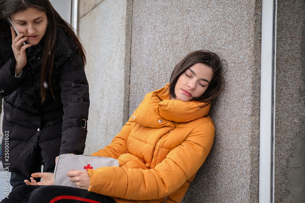 女路人在户外为昏迷的年轻女子呼叫救护车