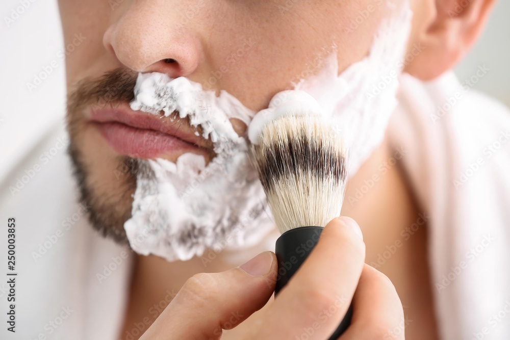 Handsome man applying shaving foam onto his face in bathroom, closeup