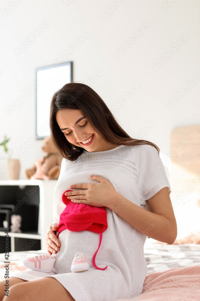 Beautiful pregnant woman with baby booties and hat in bedroom