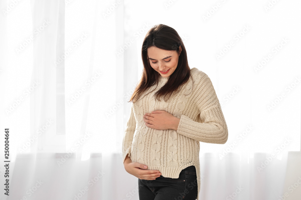 Beautiful pregnant woman near window at home