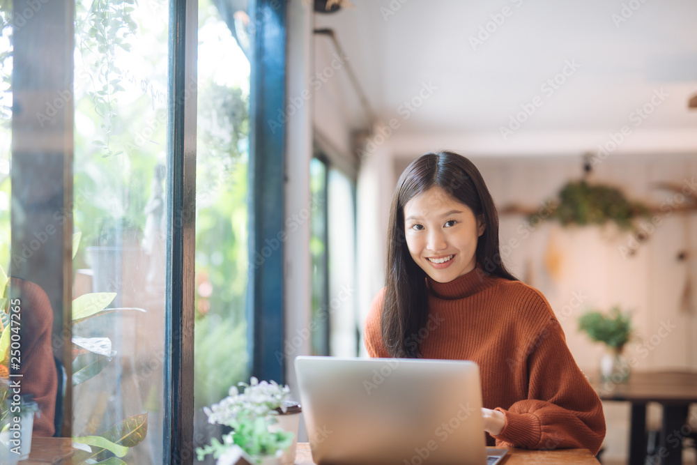 Happy young Asian girl working at a coffee shop with a laptop looking at camera.