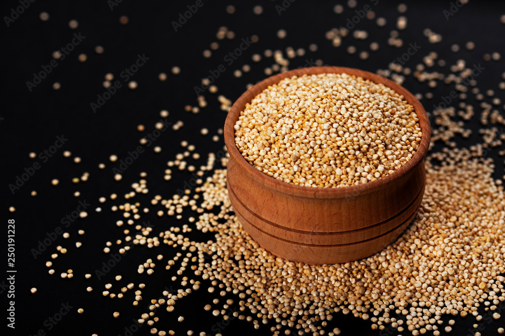 Quinoa seeds. Bowl of healthy white quinoa grains on black background, close-up