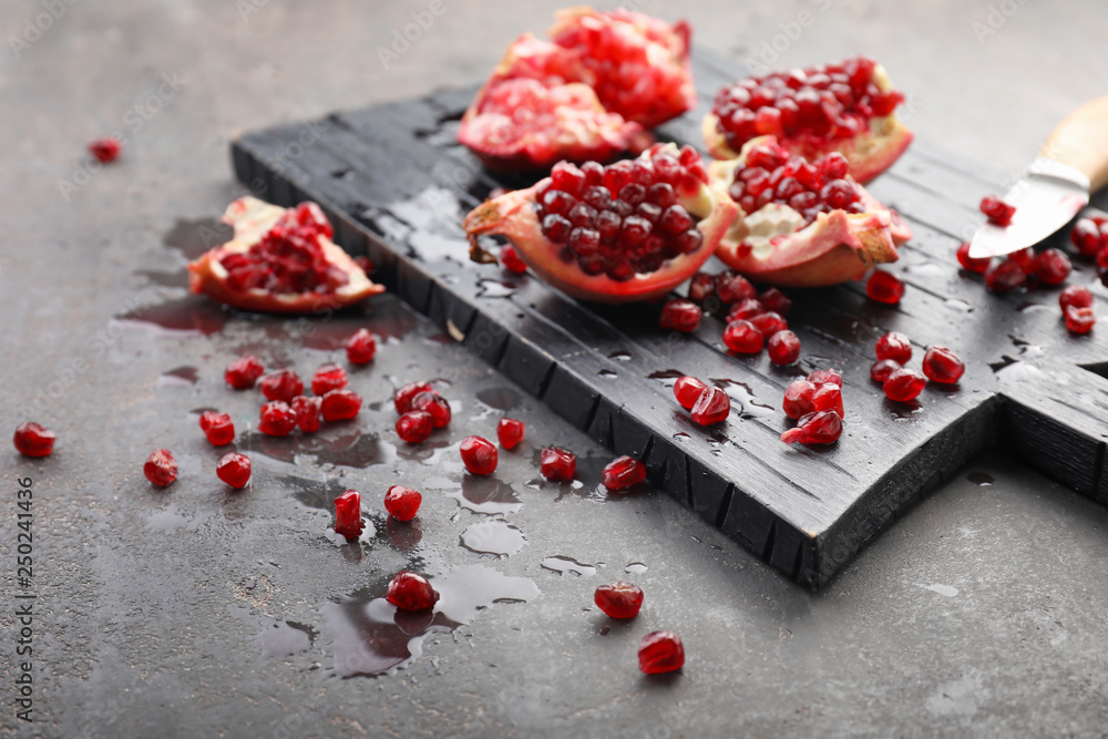 Wooden board and pieces of ripe pomegranate on grey background