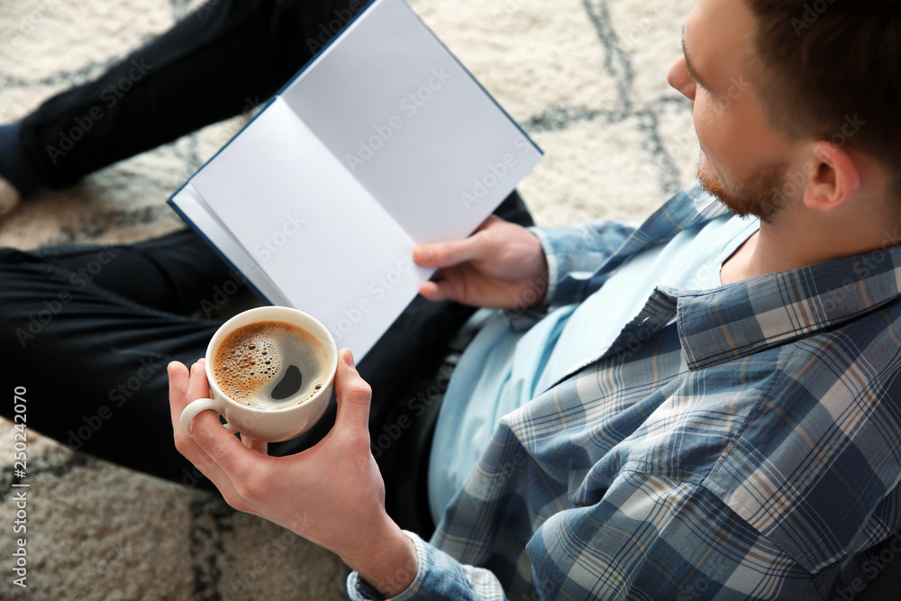 Young man drinking coffee while reading book at home