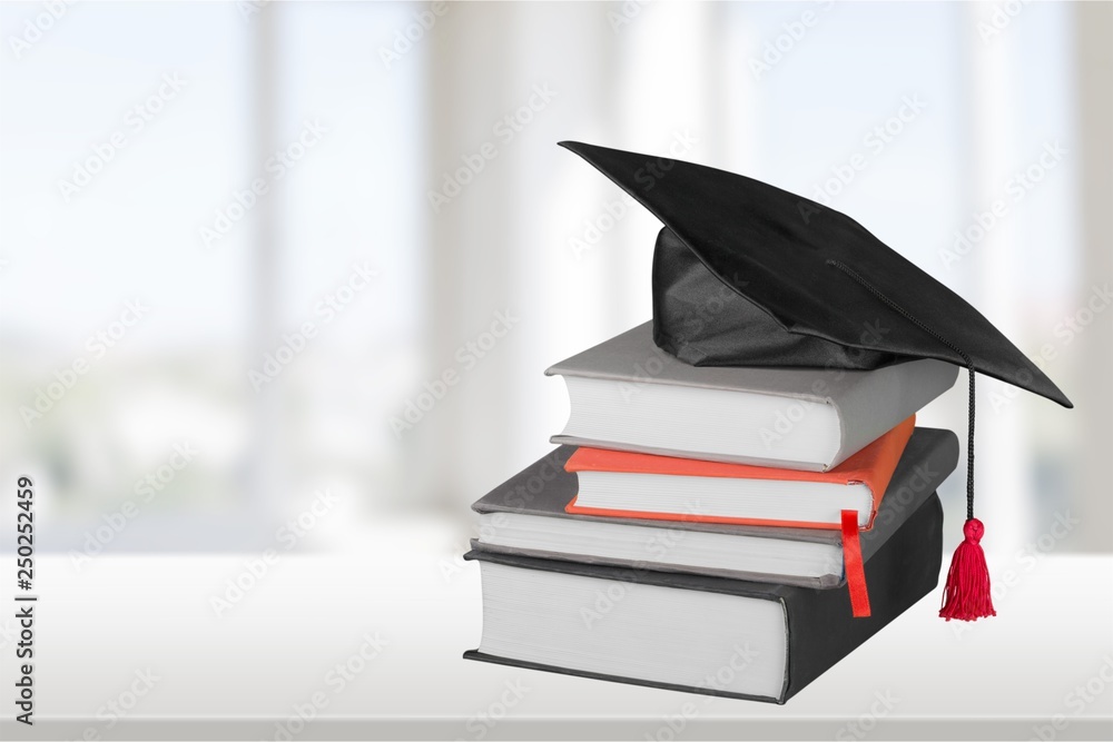 Graduation mortarboard on top of stack of books on  background