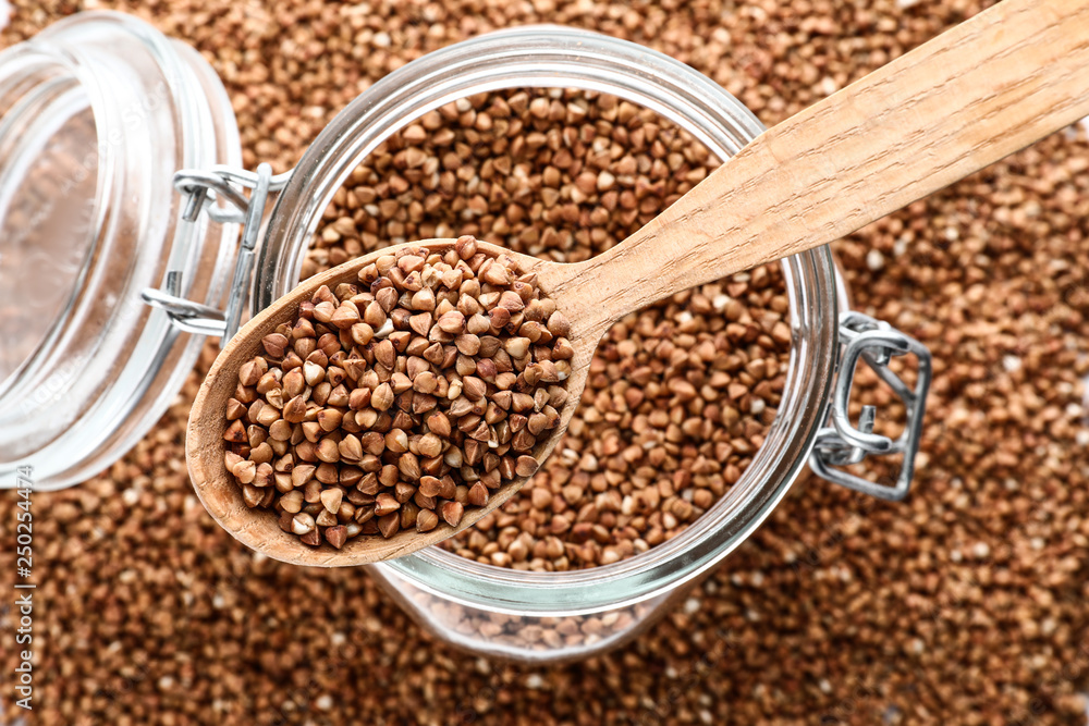 Glass jar and spoon with raw buckwheat, top view