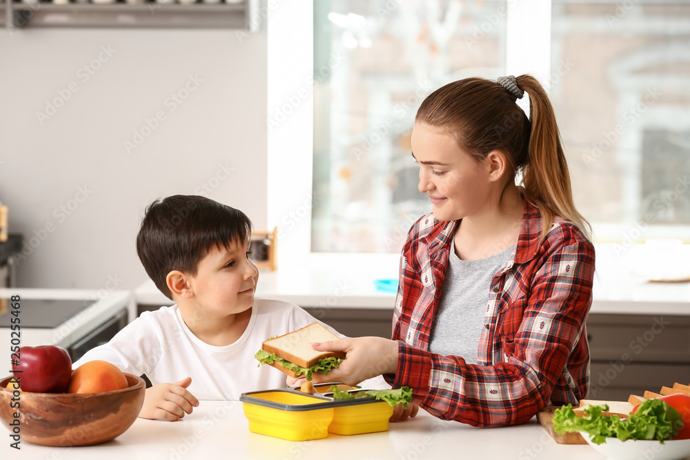 Mother packing school lunch for her little son at home