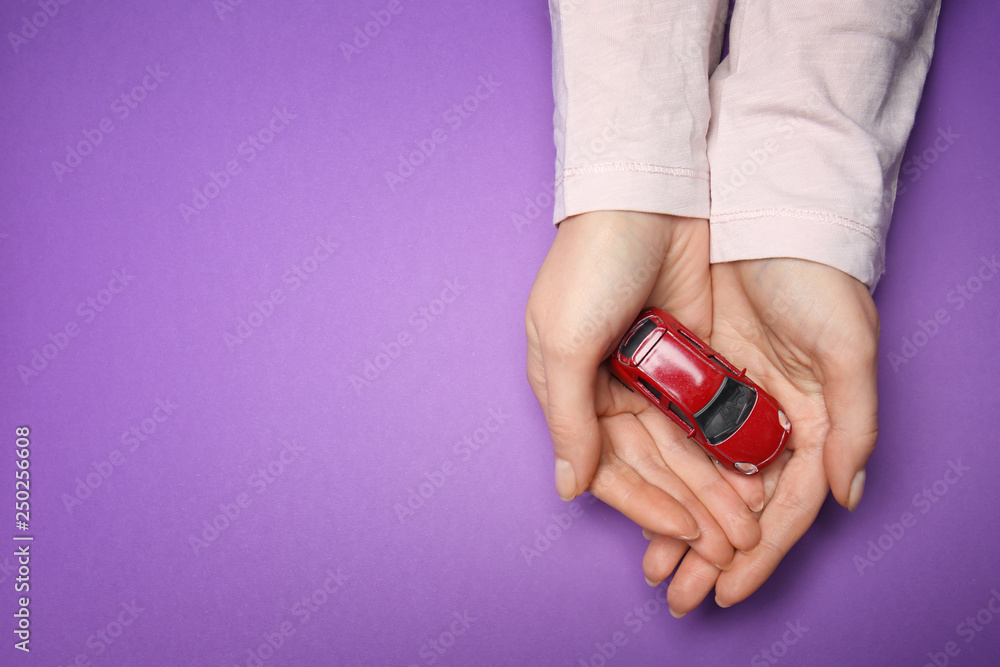 Female hands with toy car on color background. Property insurance concept