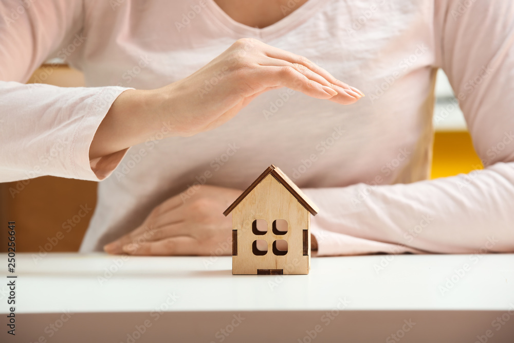 Young woman with figure of house on white table, closeup. Property insurance concept