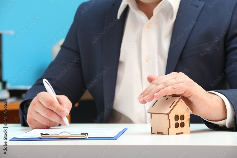 Insurance agent with figure of house sitting at table, closeup