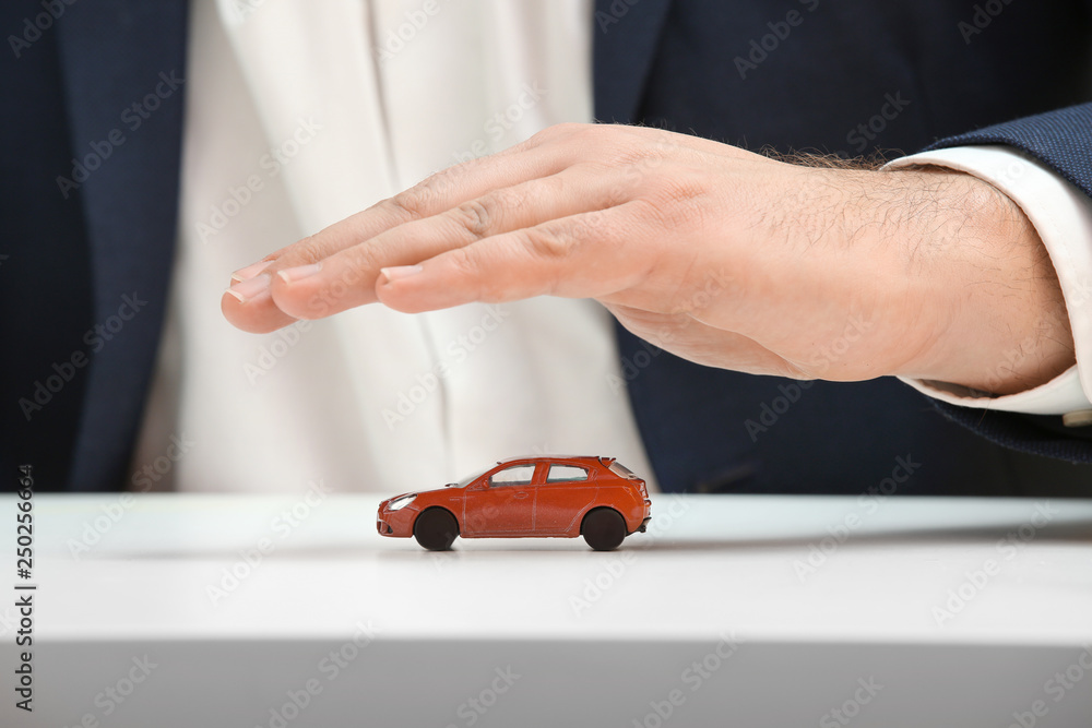 Hand of insurance agent covering toy car, closeup. Property insurance concept