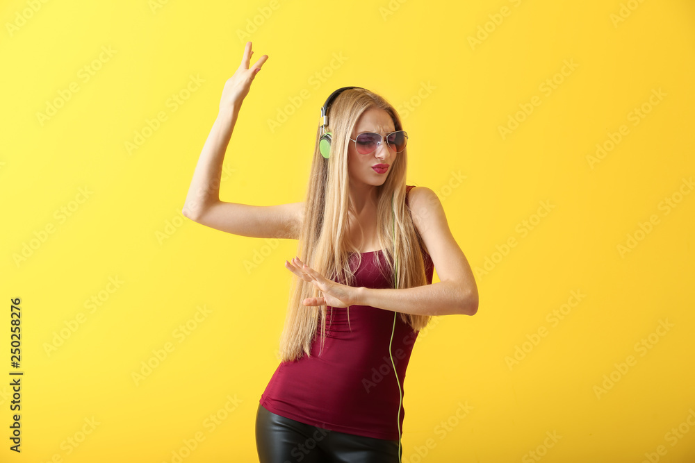 Beautiful young woman with headphones dancing against color background