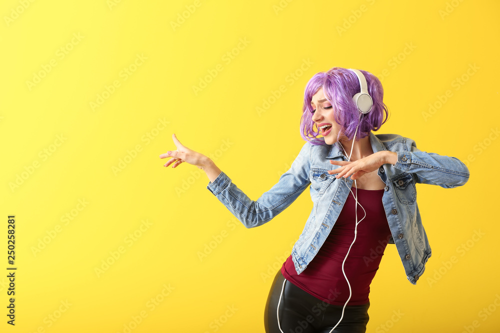 Beautiful young woman with headphones dancing against color background