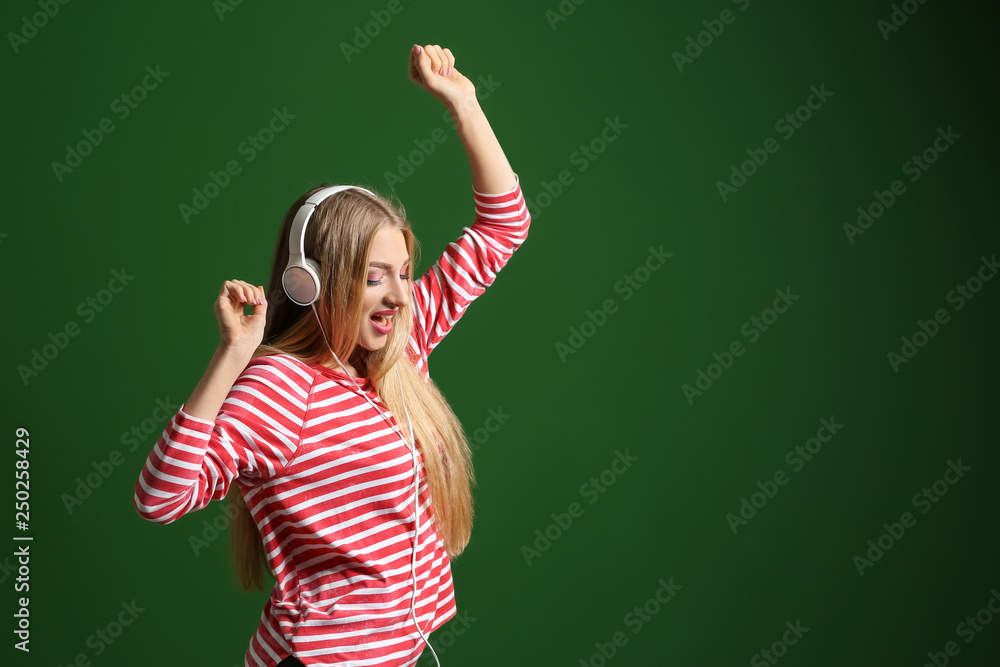 Beautiful young woman with headphones dancing against color background