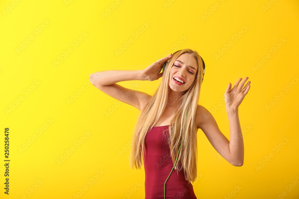 Beautiful young woman with headphones dancing against color background