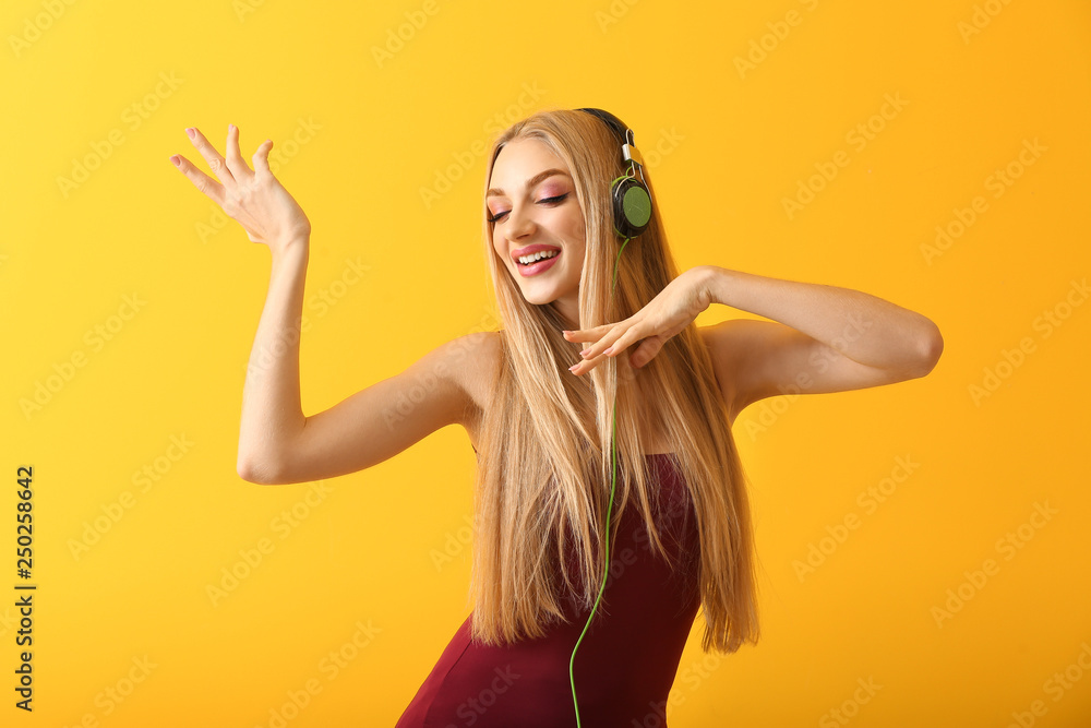 Beautiful young woman with headphones dancing against color background