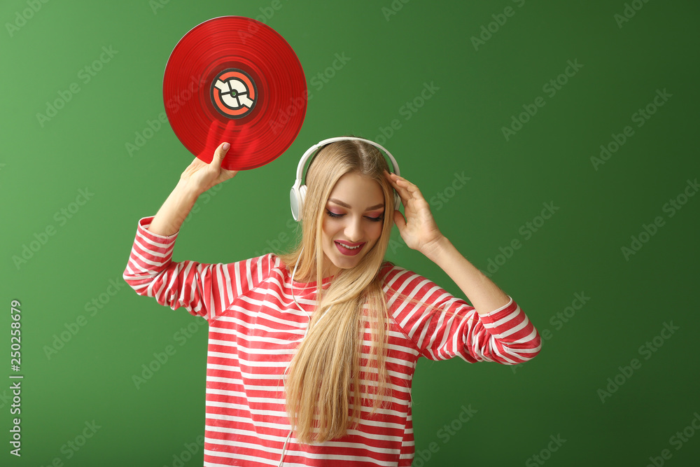 Beautiful young woman with headphones and vinyl disk  on color background