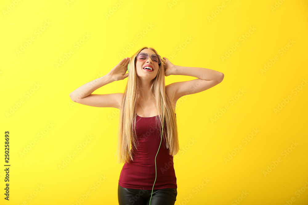 Beautiful young woman with headphones dancing against color background