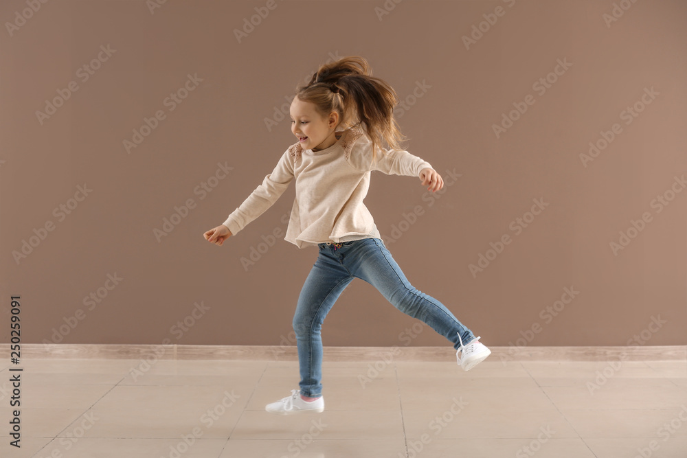 Active little girl jumping against color wall