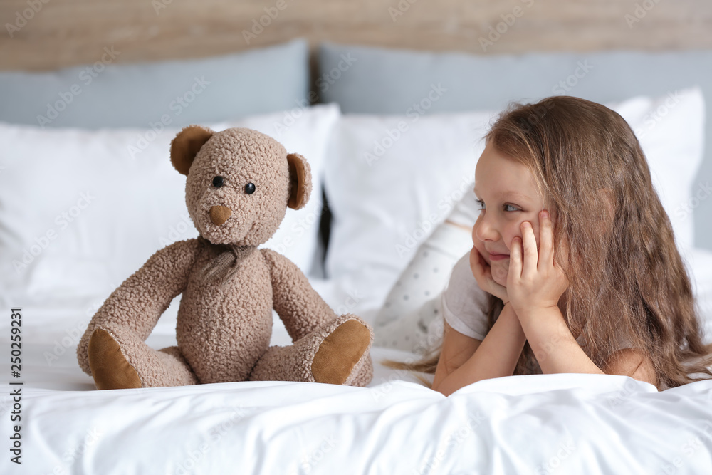 Cute little girl with toy bear lying on bed