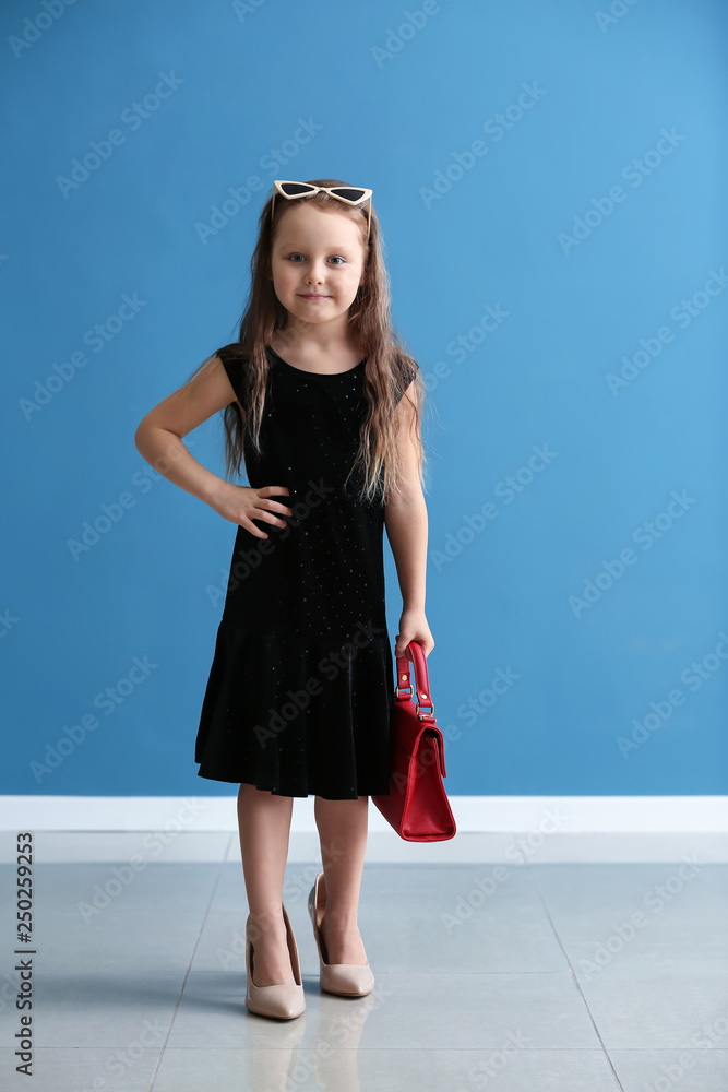 Fashionable little girl in mothers shoes against color wall