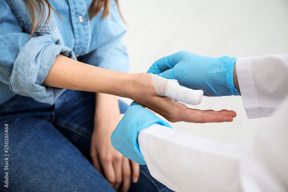 Doctor applying bandage onto finger of young woman, closeup