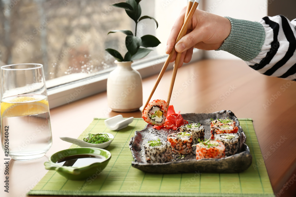 Woman eating tasty sushi rolls in cafe