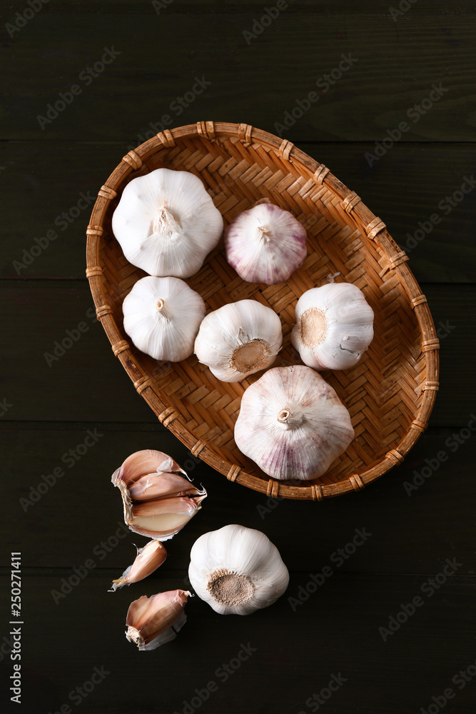 Wicker plate with fresh garlic on wooden background