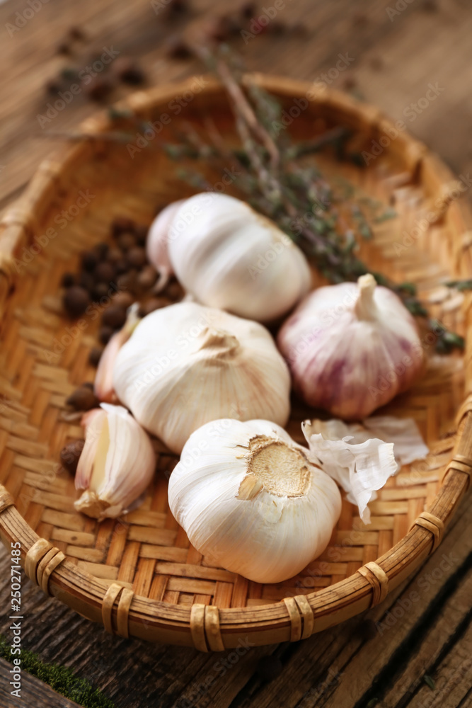 Wicker plate with fresh garlic and spices on wooden background