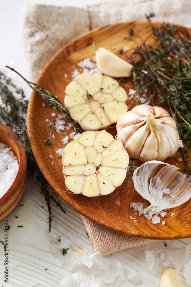 Plate with fresh garlic and thyme on white wooden background