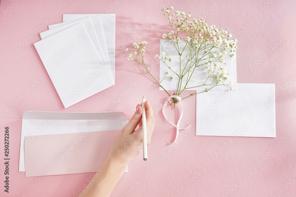 Female hand writing letter, envelopes and flowers on color background