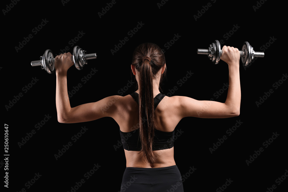 Sporty young woman with dumbbells on dark background