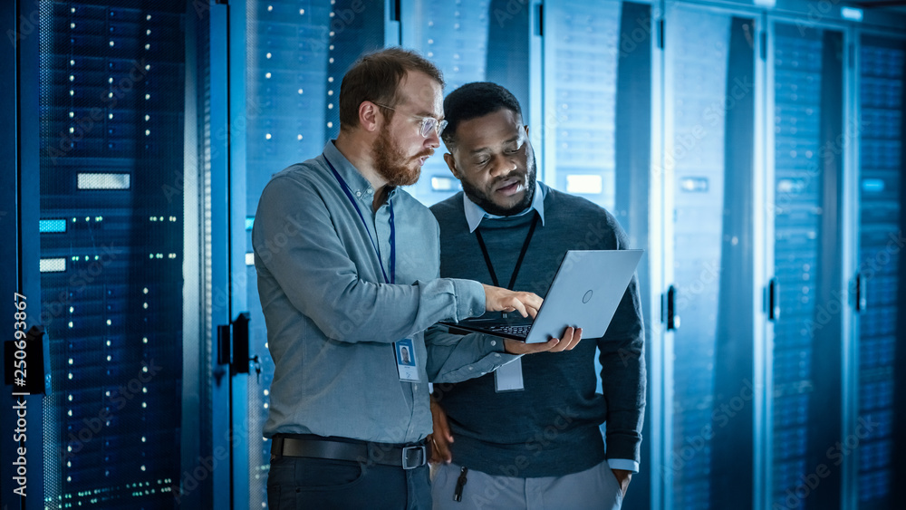 Bearded IT Technician in Glasses with Laptop Computer and Black Male Engineer Colleague are Using La