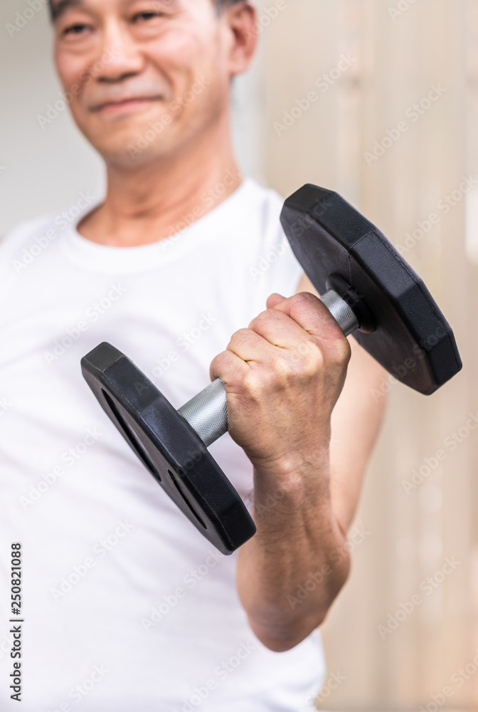 Senior man lifting dumbbell in fitness gym.