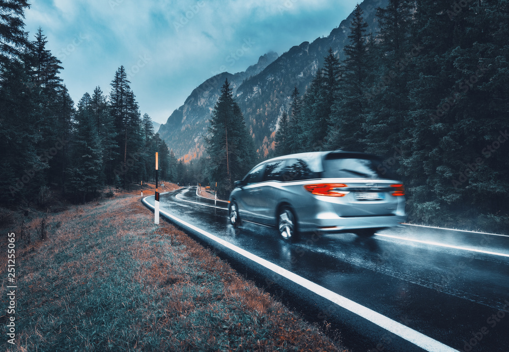 Blurred car in motion on the road in autumn forest in rain. Perfect asphalt mountain road in overcas