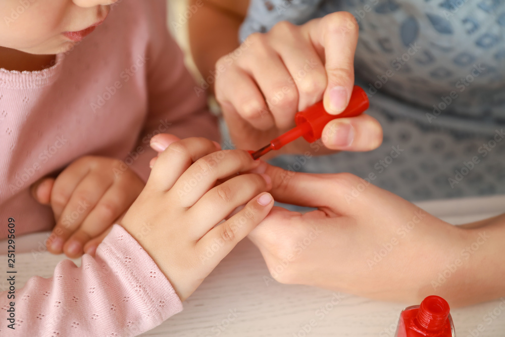 Cute daughter with mother making manicure at home, closeup