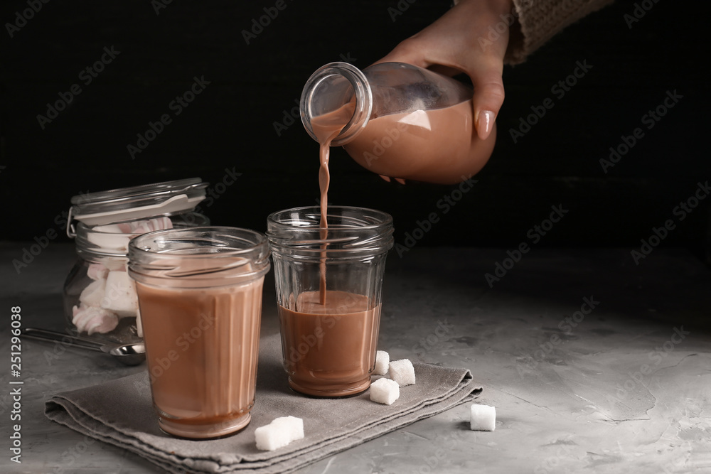 Pouring of tasty cacao drink from bottle into glass on table